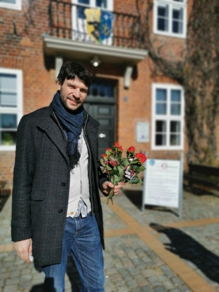 Christian Winter steht mit einigen Rosen in der Hand vor dem Ludwigsluster Rathaus.