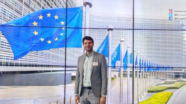 Christian Winter steht vor einem Bild, das mehrere Fahnen mit der EU-Flagge zeigt, im Gebäude der Europäischen Kommissionen.